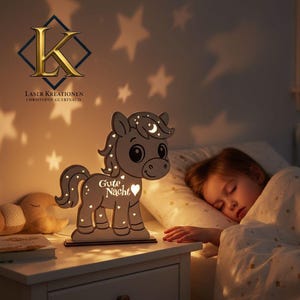 K&ouml;nnte beinhalten: Ein Nachtlicht aus Holz in Form eines Cartoon-Pferdes mit dem Text "Gute Nacht" und einem Herz. Das Pferd hat Mond- und Sternaussparungen, die Licht emittieren. Das Licht steht auf einem wei&szlig;en Nachttisch.