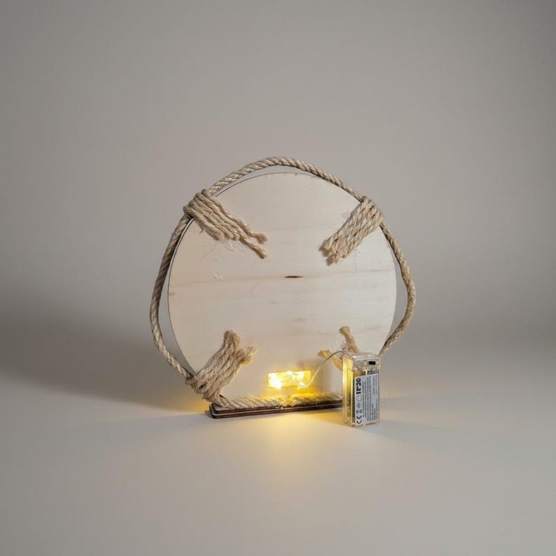 Pu&ograve; includere: Una decorazione da parete rotonda in legno con finitura legno naturale. &Egrave; circondata da una spessa corda e presenta quattro accenti di corda. Piccole luci LED bianche calde sono attaccate sul retro, alimentate da un pacco batterie.