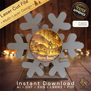 May include: A multi-layer laser cut snowflake ornament featuring a circular center with a backlit winter scene. The scene includes silhouettes of pine trees, a car with a tree on top, houses, and the text Merry Xmas. The structure is light-colored wood.