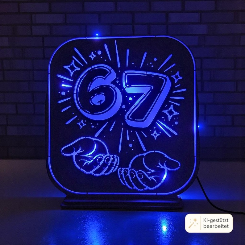 May include: A rectangular, dark-colored light box featuring a glowing blue LED design. The center displays the number 67 surrounded by radiating lines and star shapes, with two open hands illustrated below the number, all illuminated in bright blue.