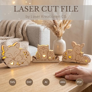 Puede incluir: Tres figuras de animales de madera iluminadas que representan un zorro, un búho y un ciervo, cada una con un pequeño recorte en forma de corazón. El texto LASER CUT FILE by Laser Kreationen CG es visible arriba, con iconos SVG, DXF, AI, LBRN2 y PDF.
