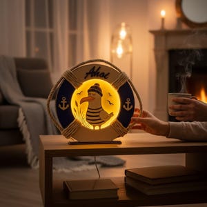 Pu&ograve; includere: Lampada decorativa a forma di salvagente, con un design a gabbiano dei cartoni animati. La lampada emette una luce gialla calda e presenta la scritta "Ahoj". Posizionata su un tavolo di legno, crea un'atmosfera accogliente.