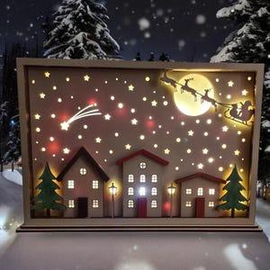 May include: A wooden Christmas scene light-up decoration featuring a snowy village, a shooting star, and Santa Claus flying in a sleigh pulled by reindeer. The scene is illuminated with warm white LED lights.