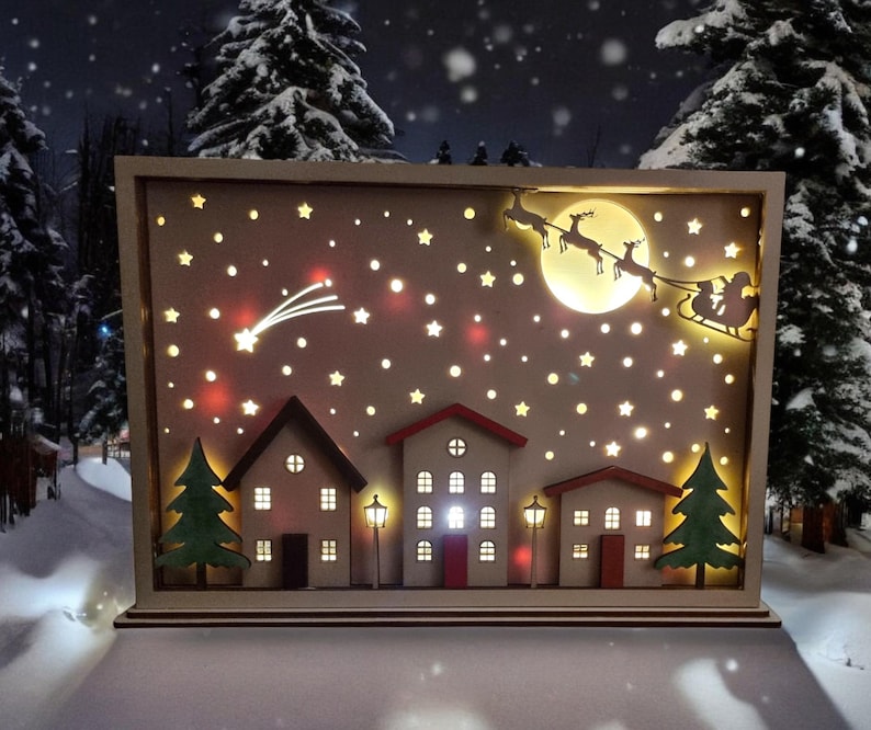 May include: A wooden Christmas scene light-up decoration featuring a snowy village, a shooting star, and Santa Claus flying in a sleigh pulled by reindeer. The scene is illuminated with warm white LED lights.