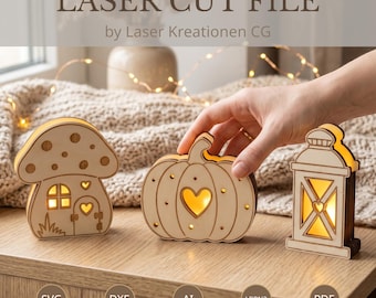 May include: Three light-colored wooden laser-cut decorations featuring a mushroom house, a pumpkin with a heart cutout, and a lantern. Each piece is illuminated from within, casting a warm glow through the cutouts on a wooden surface.