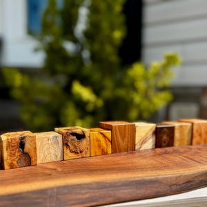 May include: A row of eight small wooden blocks, each with a unique wood grain pattern and color, arranged on a dark brown wooden surface.