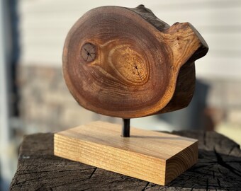 Könnte beinhalten: Eine Holzskulptur aus einer Baumscheiben-Scheibe mit natürlicher Holzmaserung. Die Skulptur ist auf einem kleinen Holzsockel montiert.