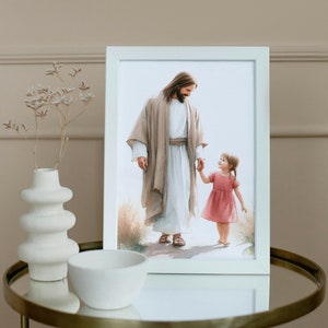May include: A framed watercolor painting of a man in a white robe holding the hand of a little girl in a pink dress. The man is looking down at the girl with a kind expression. The painting is set against a white background.
