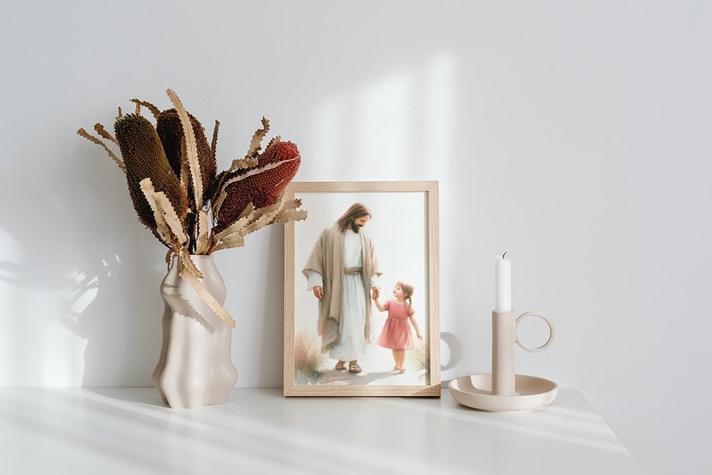 May include: A framed print of a painting depicting Jesus walking with a young girl. The print is on a white shelf with a vase of dried flowers and a candle holder.