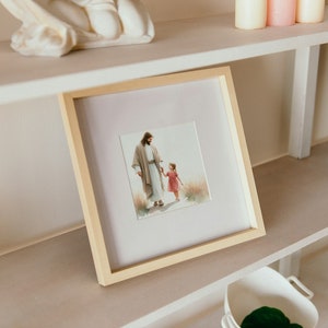 May include: A framed picture of a man in a white robe holding a young girl's hand. The picture is on a white shelf with other decorative items.