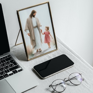 May include: A gold-framed picture of Jesus walking with a young girl, a laptop, a smartphone, and eyeglasses on a white surface.