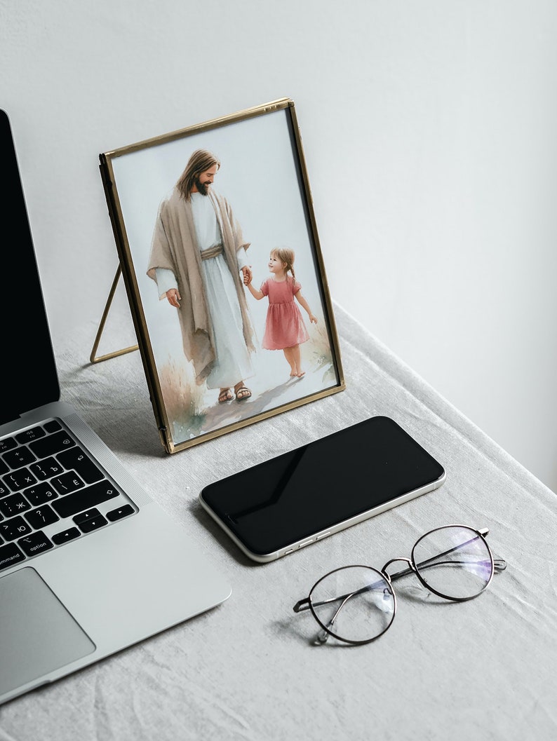 May include: A gold-framed picture of Jesus walking with a young girl, a laptop, a smartphone, and eyeglasses on a white surface.