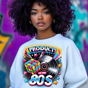 May include: A white sweatshirt with a colorful graphic design featuring the text "Products of the 80s" with a Rubik's Cube, a vinyl record, and stars.