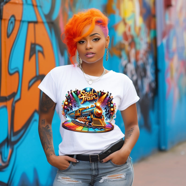 May include: White t-shirt with a colorful graphic of a train, the words "Soul Train", and a rainbow-colored track. The shirt is worn with blue jeans and a black belt. The background features graffiti art.