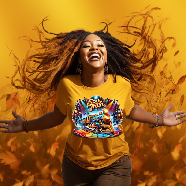 May include: Mustard yellow t-shirt with a colorful "Soul Train" graphic featuring a train, stage lights, and a rainbow platform. The person is smiling with arms outstretched, set against a yellow background with falling leaves.