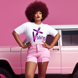 May include: A white t-shirt with the word "Victory" in a purple and pink design. The model is wearing pink shorts and standing in front of a pink car. The background is a solid pink color.