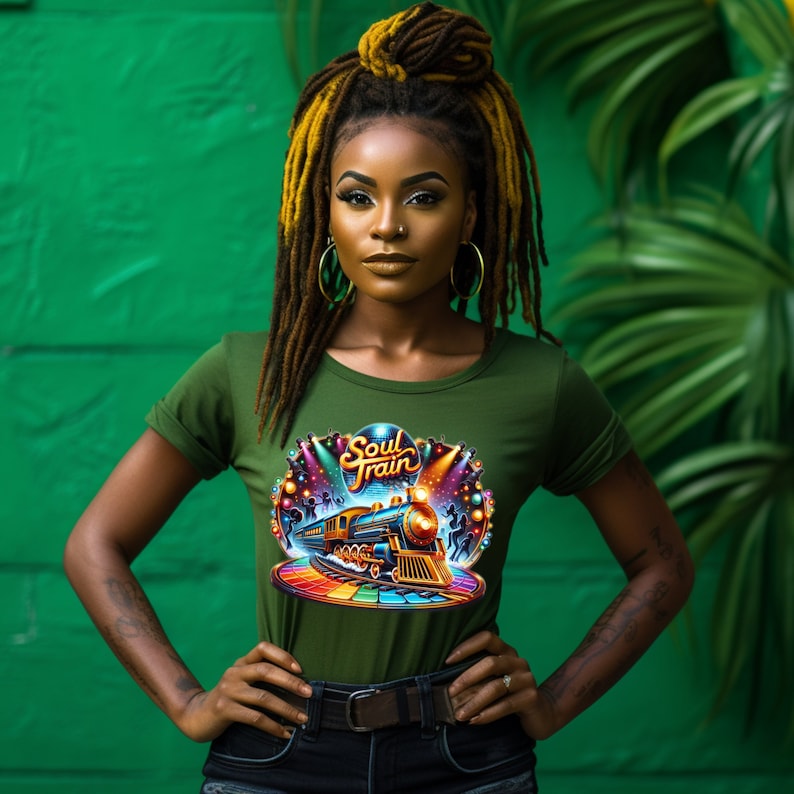 May include: Olive green t-shirt with a colorful "Soul Train" graphic featuring a train, dancers, and stage lights. The shirt has a crew neck and rolled-up sleeves. The background is a vibrant green.