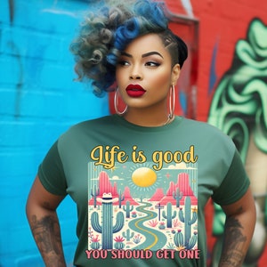 May include: A green t-shirt with a graphic of a desert landscape with cacti and a road. The text "Life is good" is above the graphic and "You should get one" is below the graphic.