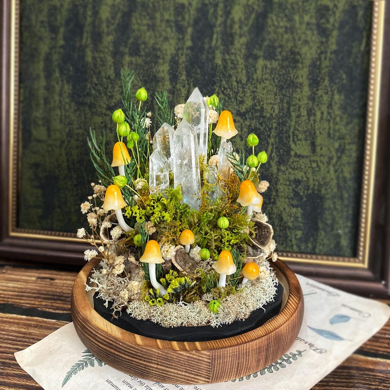 May include: A miniature forest scene with clear quartz crystals, moss, and small yellow mushrooms in a wooden circular planter.