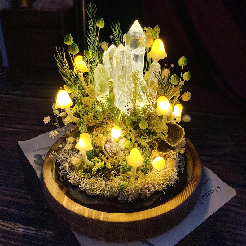 May include: A crystal and mushroom fairy garden with glowing lights. The crystal tower is surrounded by moss, small plants, and mushrooms with glowing lights.