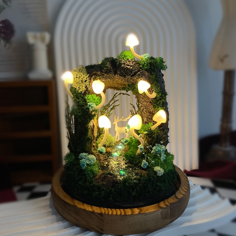 May include: A miniature forest scene with a wooden base and a deer figurine. The scene is lit by small, white, mushroom-shaped lights.