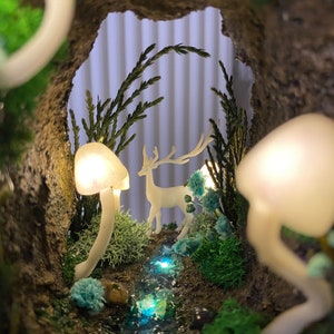 May include: A miniature forest scene with a white deer figurine, a small stream, and glowing white mushrooms. The scene is set inside a rock cave with green foliage.