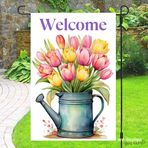 May include: A garden flag with the word "Welcome" in purple script. The flag features a watercolor illustration of a bouquet of pink, yellow, and orange tulips in a blue watering can. The flag is displayed on a black metal stand.