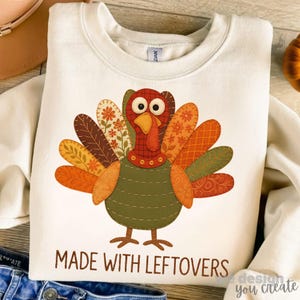 May include: Cream sweatshirt with a turkey design and the text "MADE WITH LEFTOVERS". The turkey is made of patchwork with orange, brown, and green colours. A festive top for the Thanksgiving holiday.