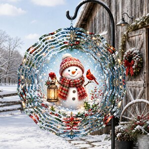 May include: A circular metal wind spinner featuring a central illustration of a snowman wearing a red patterned hat and scarf, holding a lit lantern, with a red cardinal perched on its arm, surrounded by holly, snowflakes, and a blue background.