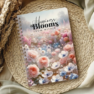 May include: A spiral bound journal with a floral design and the text "Happiness Blooms From Within". The cover features a variety of pink, white, and blue flowers.