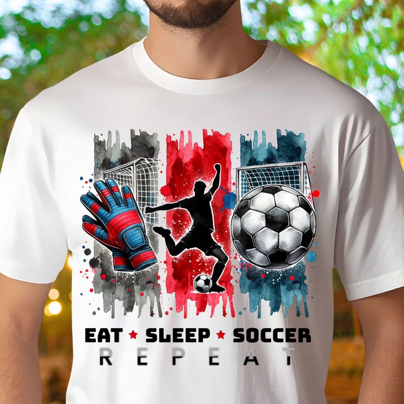 May include: White t-shirt with a watercolor design of a soccer player, a soccer ball, and a pair of goalie gloves. The text "Eat Sleep Soccer Repeat" is printed below the design.
