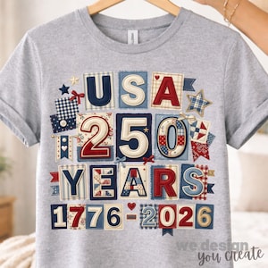 Puede incluir: Una camiseta gris con un diseño patriótico que celebra los 250 años de EE. UU. El diseño presenta el texto "USA 250 YEARS 1776-2026" en un estilo patchwork con colores rojo, blanco y azul. La camiseta está colgada en una percha de madera.