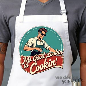 May include: White apron with a retro-style design featuring a man in sunglasses cooking. The text reads "Mr Good Lookin' is Cookin'".