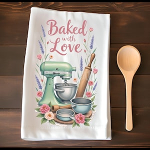 K&ouml;nnte beinhalten: Wei&szlig;es K&uuml;chentuch mit dem Text "Baked with Love" in rosa Schrift. Das Tuch zeigt einen mintgr&uuml;nen K&uuml;chenmixer, ein Nudelholz und Sch&uuml;sseln, umgeben von rosa Rosen und Lavendelzweigen. Ein Holzl&ouml;ffel liegt auf einer dunklen Holzoberfl&auml;che.
