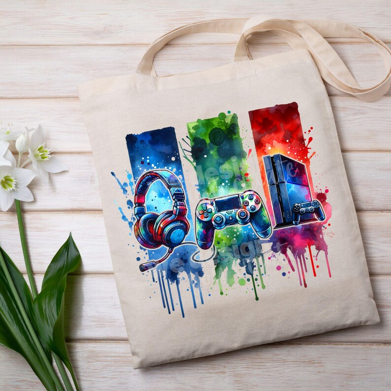 May include: A white canvas tote bag with a colorful design of a video game controller, headphones, and a game console. The design is in a watercolor style with splashes of color.