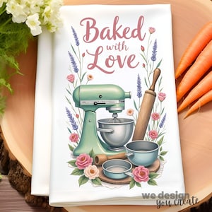 May include: White kitchen towel with a design featuring a mint green stand mixer, rolling pin, and bowls, surrounded by pink roses and lavender. The text "Baked with Love" is displayed in pink script. The towel is on a wooden surface.