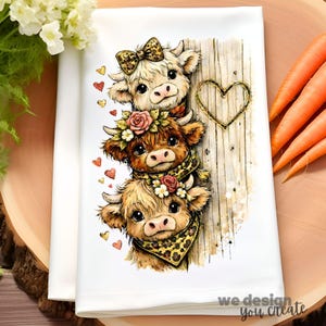 May include: White kitchen towel featuring a stack of three cartoon cows with floral and leopard print accents. The cows are adorned with bows, flower crowns, and bandanas. A wooden heart and the text "we design you create" are also visible.