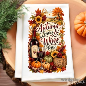 May include: A white kitchen towel featuring a colorful autumn-themed illustration with a wine bottle, a wine glass, pumpkins, sunflowers, and fall foliage. The text reads Autumn Leaves & Wine Please, Good Friends Good Wine Good Times, and Grateful Thankful Blessed.