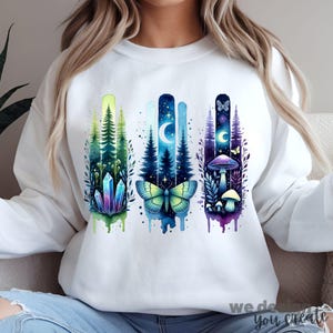 May include: White sweatshirt with a watercolor design of three vertical panels. Each panel features a different nature scene: crystals, a butterfly, and mushrooms. The design is in shades of blue, green, and purple.