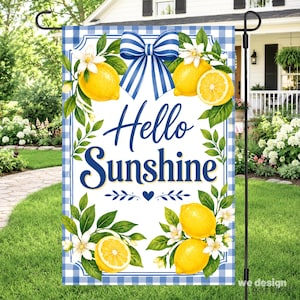 May include: A rectangular garden flag featuring a blue and white gingham border, a central blue bow, and yellow lemon illustrations with white blossoms. The text "Hello Sunshine" is printed in blue script and serif fonts in the center.