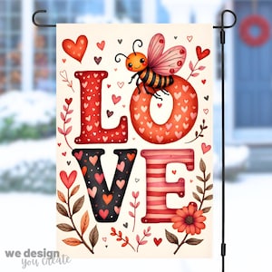 May include: A garden flag with the word "LOVE" in red and black letters, decorated with hearts and floral accents. A cartoon bee sits atop the letter "O". The flag has a cream background and the text "we design you create".