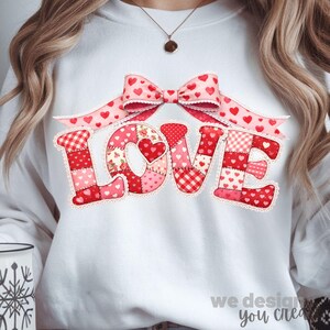 May include: White sweatshirt featuring the word "LOVE" in a patchwork design with red and pink hearts and patterns. A pink bow with heart accents sits above the word. The text "we design you create" is at the bottom.