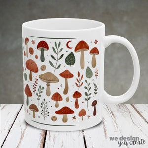 Puede incluir: Taza de cerámica blanca con un patrón colorido de setas y hojas. La taza tiene un asa redondeada.