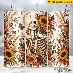 May include: A cylindrical tumbler with a straw featuring a cream background, a central human skeleton, sunflowers, autumn leaves, wheat stalks, red berries, and a butterfly. The design includes star accents and a crescent moon shape behind the skull.