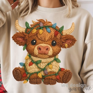 May include: A beige sweatshirt featuring a detailed illustration of a Highland cow adorned with a string of colorful Christmas lights. The cow is brown with a cream-colored sweater, and the lights are red, yellow, blue, and green. The text "we design you create" is at the bottom right.