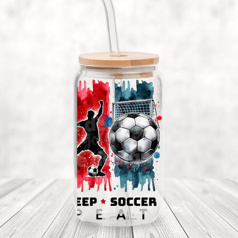 May include: A clear glass tumbler with a bamboo lid and a straw. The tumbler has a watercolor design of a soccer player, a soccer ball, and a goal. The text "Keep Soccer Real" is printed on the bottom of the tumbler.