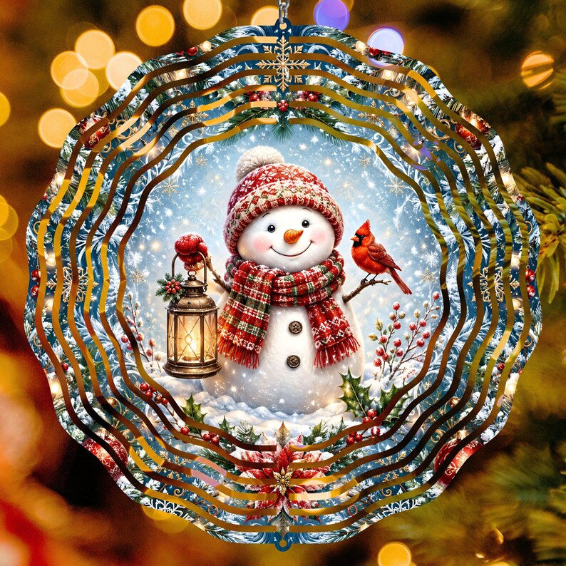 May include: A circular metal wind spinner featuring a snowman wearing a red patterned hat and scarf, holding a lit lantern. A red cardinal sits on a branch next to the snowman. The design includes holly, berries, and snowflakes on a blue background.