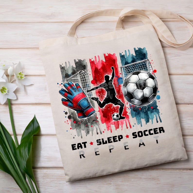 May include: A white canvas tote bag with a watercolor design of a soccer player, a soccer ball, and a goal. The text "Eat Sleep Soccer Repeat" is printed on the bag.