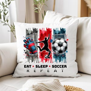 May include: White pillow with a watercolor design of a soccer player, a soccer ball, and a pair of goalie gloves. The text "Eat * Sleep * Soccer Repeat" is printed below the design.