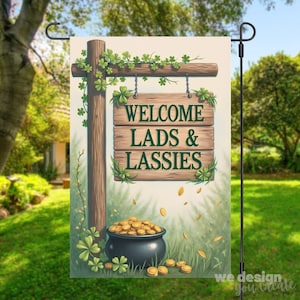 May include: A St. Patrick's Day garden flag featuring a wooden sign that reads "WELCOME LADS & LASSIES." The sign is decorated with shamrocks and hangs above a pot of gold. The flag is displayed on a black metal stand.